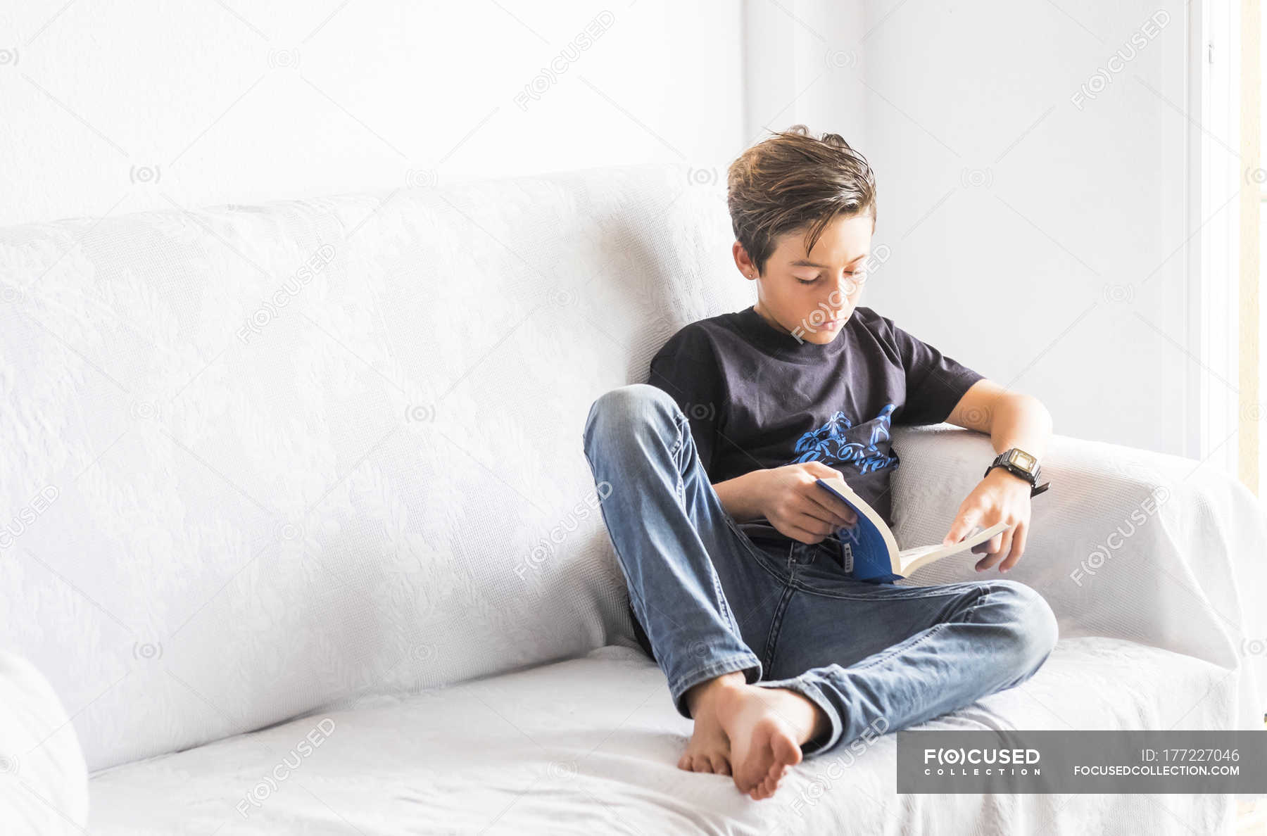 Boy Sitting On A White Couch Reading A Book Male Looking Down