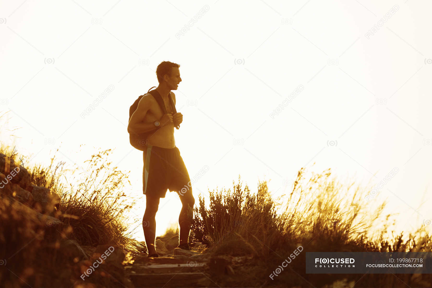 Bare Chested Male Hiker With Backpack On Trail At Sunset Side View