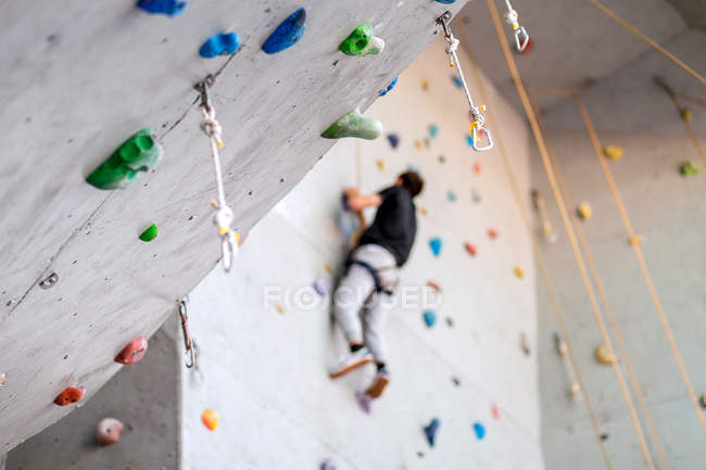 Mann klettert an praktischer Wand drinnen, sichert Karabiner und Seil — Stockfoto