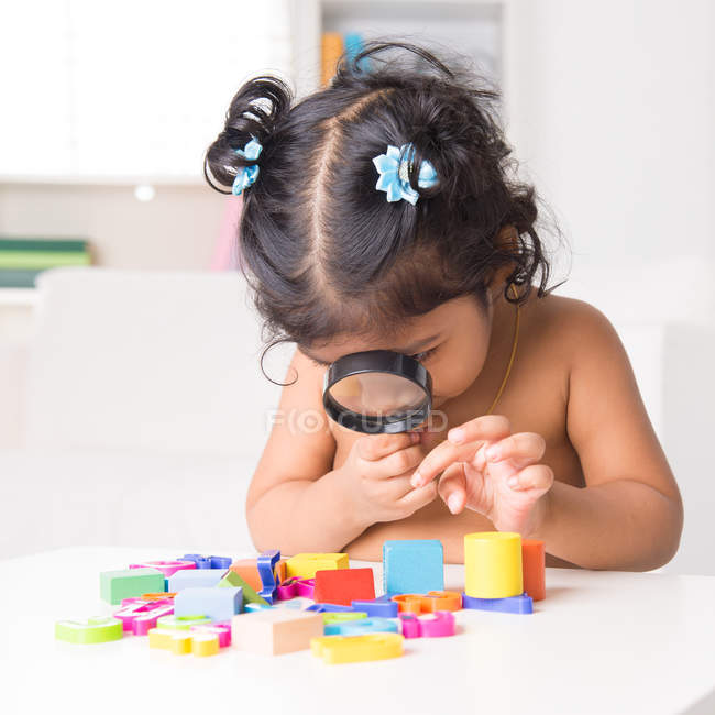 Indian girl zoom into toys through a magnifying glass — Stock Photo