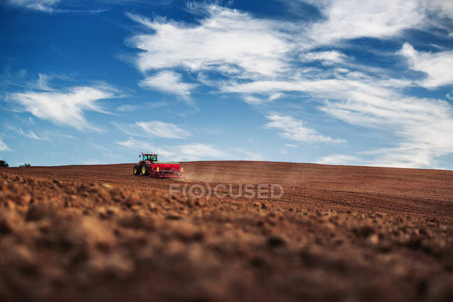 Farmer with tractor seeding crops at field — Stock Photo