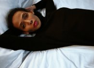 Woman laying on white sheets and looking at camera — Stock Photo