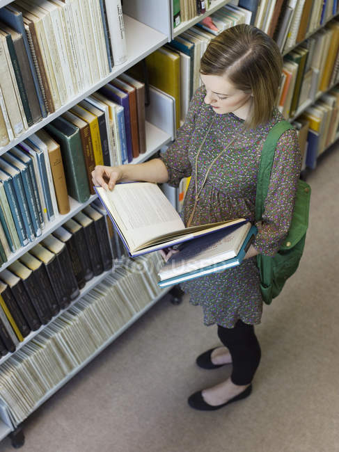 Femme regardant le livre dans la bibliothèque — Photo de stock