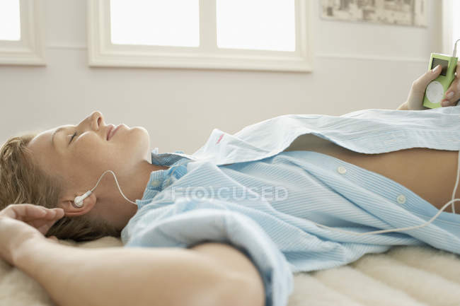 Mujer en la cama escuchando música - foto de stock