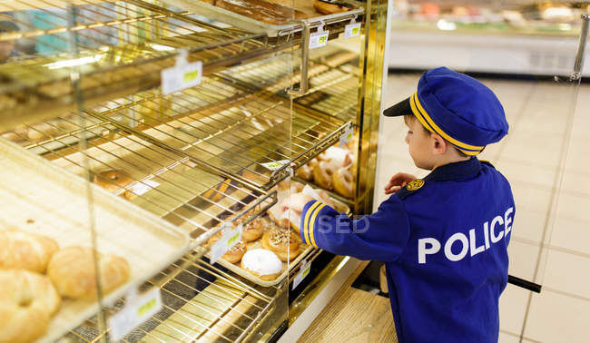 Niño en traje de policía elegir bollos - foto de stock