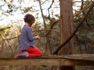 Girl sitting on wooden surface between trees — Stock Photo