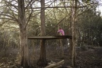 Дівчина сидить на дерев'яній поверхні між деревами — стокове фото
