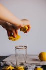 Mãos de colheita espremendo metades de limão em vidro — Fotografia de Stock