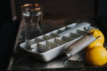 Bodegón de bandeja de hielo vintage y vaso de agua con limones - foto de stock