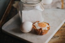 Close up view of baked egg basket and raw egg on marble cutting board — Stock Photo