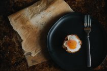 Direkt über Ansicht des gebackenen Eierkorbs auf schwarzem Teller mit Gabel — Stockfoto