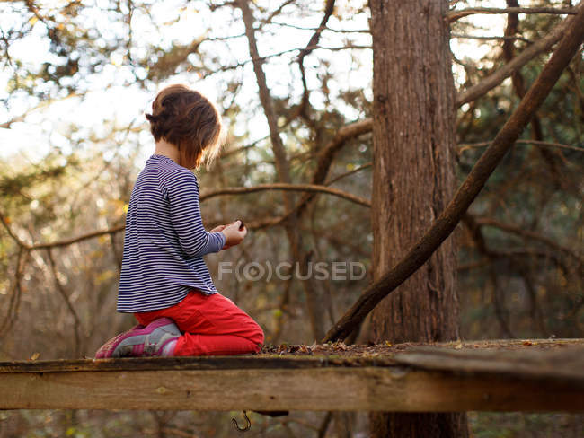Menina sentada na superfície de madeira entre árvores — Fotografia de Stock