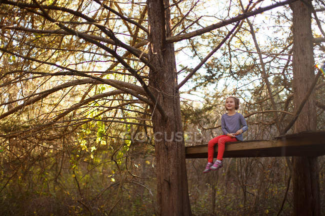 Girl sitting on wooden surface between trees — Stock Photo