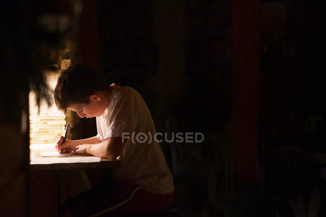 Хлопчик пише листа в темній кімнаті — стокове фото