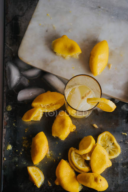 Directly above view of glass of lemonade on table with lemon peels and ice — Stock Photo
