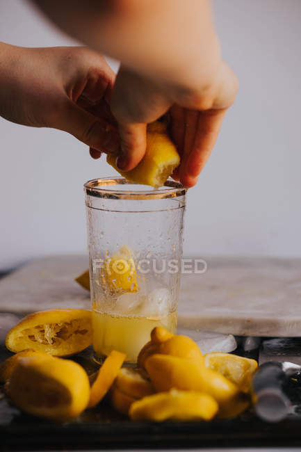 Mãos de colheita espremendo limão metade em vidro — Fotografia de Stock