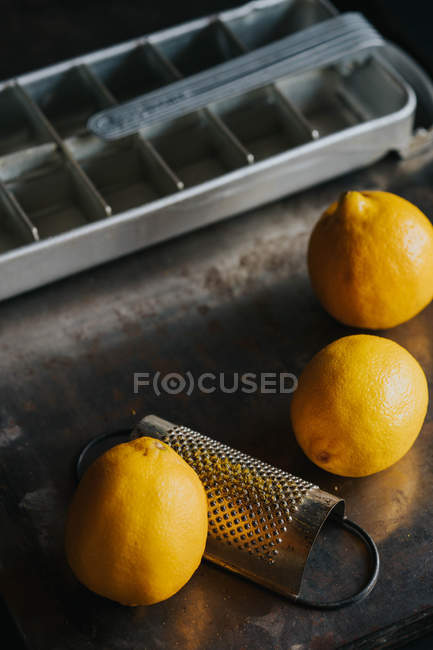 Vue rapprochée des citrons avec râpe par plateau de glace — Photo de stock