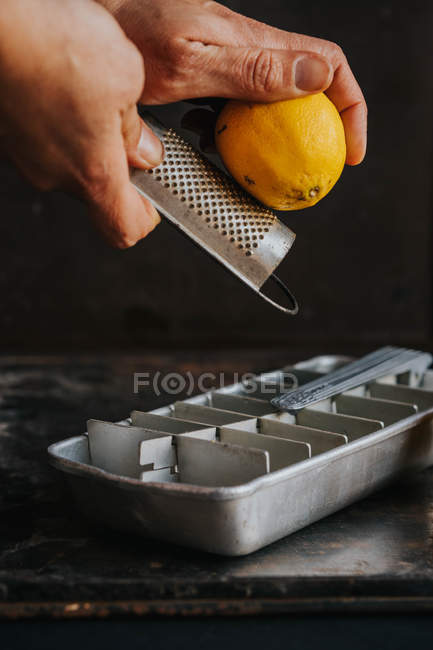 Manos de cultivo rallado ralladura de limón en bandeja de hielo - foto de stock