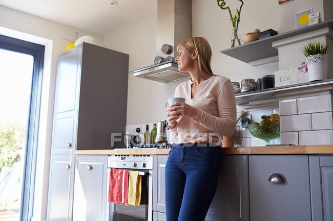 Femme debout dans la cuisine avec boisson chaude — Photo de stock