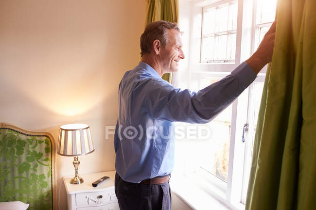 Uomo anziano aprendo tende — Foto stock