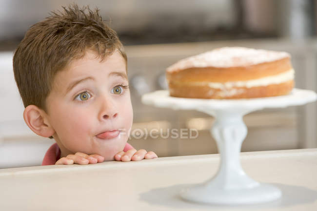 Boy staring longingly at cake at home licking lips — Stock Photo