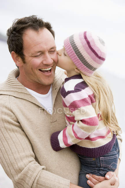 Padre sosteniendo hija besándolo en la playa sonriendo - foto de stock