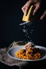 Human hand grating cheese on pasta — Stock Photo