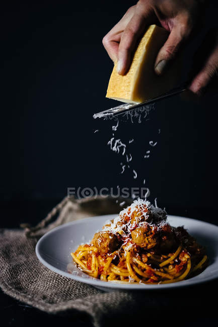 Menschliche Hand, die Käse auf Nudeln reibt — Stockfoto