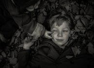 Niño acostado en hojas - foto de stock