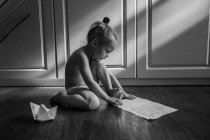 Mädchen sitzt auf dem Boden und bastelt Papierboote — Stockfoto