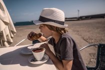 Хлопчик їсть круасан з кавою — стокове фото