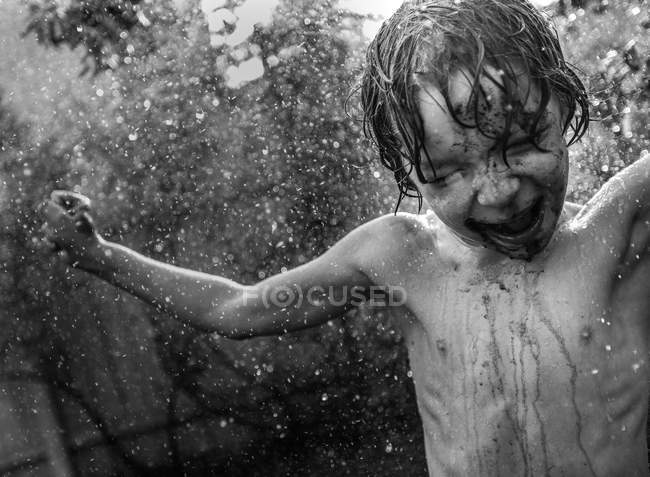 Boy under watering splashes — Stock Photo