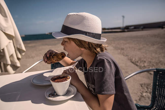 Хлопчик їсть круасан з кавою — стокове фото