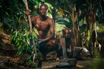 Africano hombre e hijo agachándose en el bosque - foto de stock