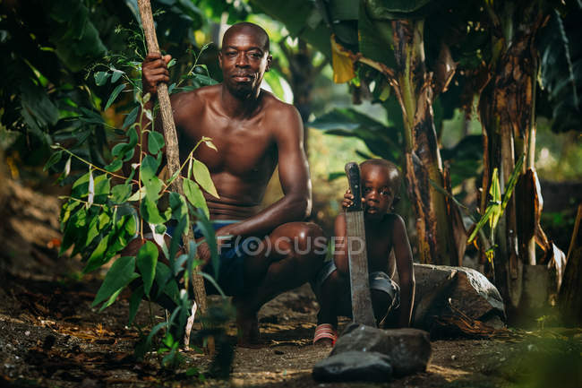 Africano hombre e hijo agachándose en el bosque — Stock Photo