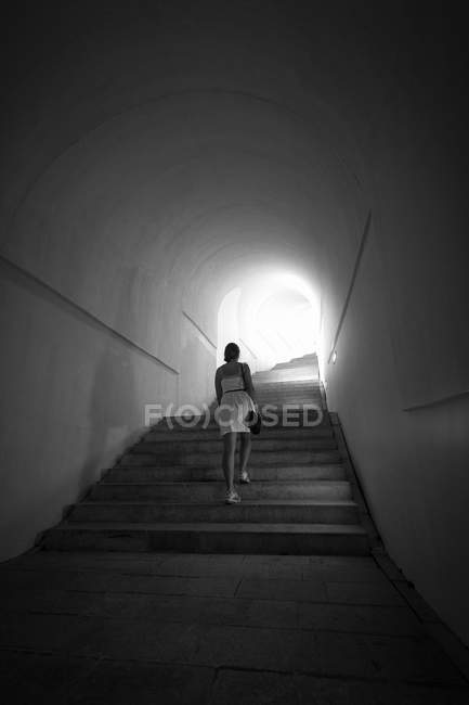 Woman going up the stairs at tunnel with light in the end — Stock Photo