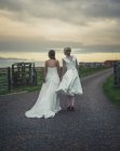 Amante casal lésbico de pé na estrada, de mãos dadas. Casamento de casal gay, Kinkell Byre, St Andrews, Escócia, Reino Unido, 2013 — Fotografia de Stock