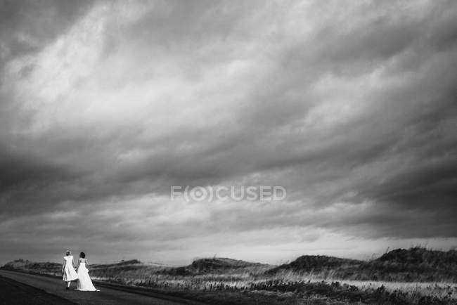 Casal lésbico amoroso andando na estrada, entre colinas, de mãos dadas. Casamento de casal gay, St Andrews, Escócia, Reino Unido, 2013 — Fotografia de Stock