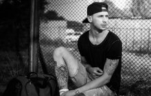 Tattooed man sitting near fence — Stock Photo
