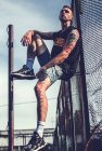 Tatuato uomo seduto su metallo costruzione — Foto stock