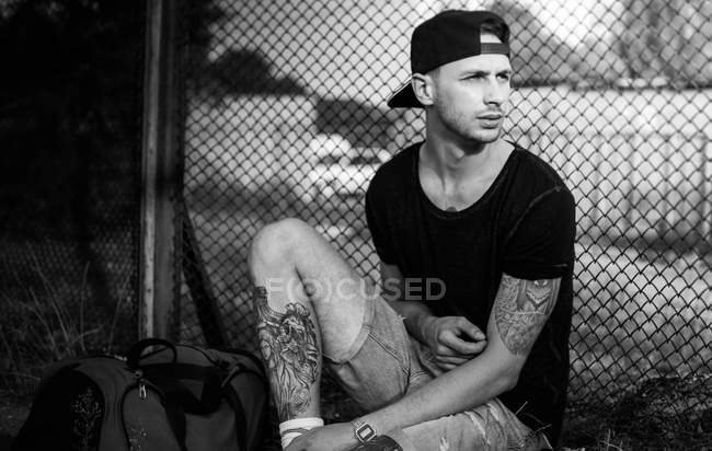 Uomo tatuato seduto vicino alla recinzione — Foto stock