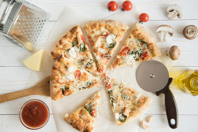 Pizza rebanada con queso y utensilios de cocina - foto de stock