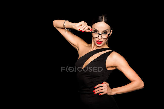 Femme séduisante en robe bodycon noire et lunettes design sur fond noir — Photo de stock