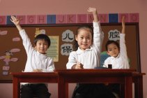 Estudantes em classe levantando as mãos — Fotografia de Stock