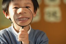 Schoolboy showing teeth in magnifying glass — Stock Photo