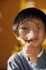 Schoolboy looking at camera with magnifying glass — Stock Photo