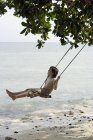 Boy swinging near ocean — Stock Photo