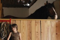 Мальчик в конюшне рядом с лошадью — стоковое фото