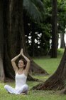 Woman doing yoga exercises under trees — Stock Photo