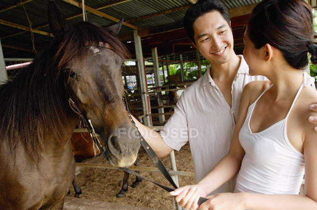 Coppia in stalla in piedi con cavallo — Foto stock